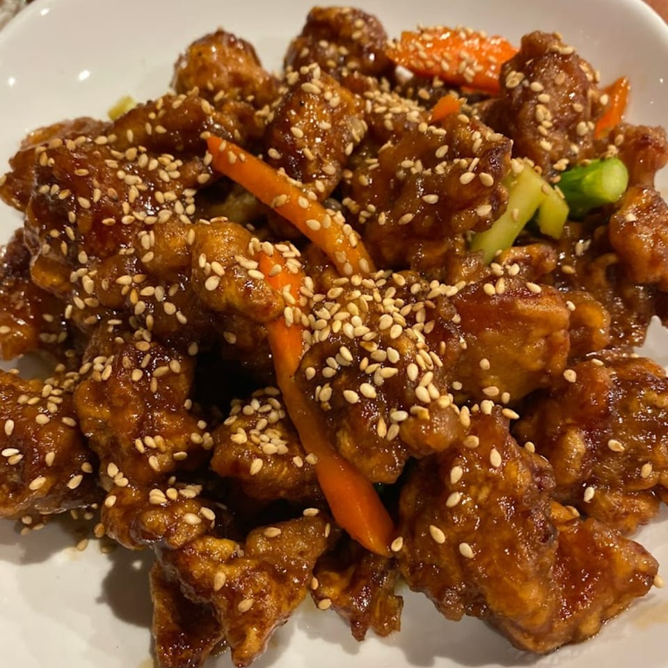 Sesame chicken with carrots and green onions, glistening with sauce, on a white plate.