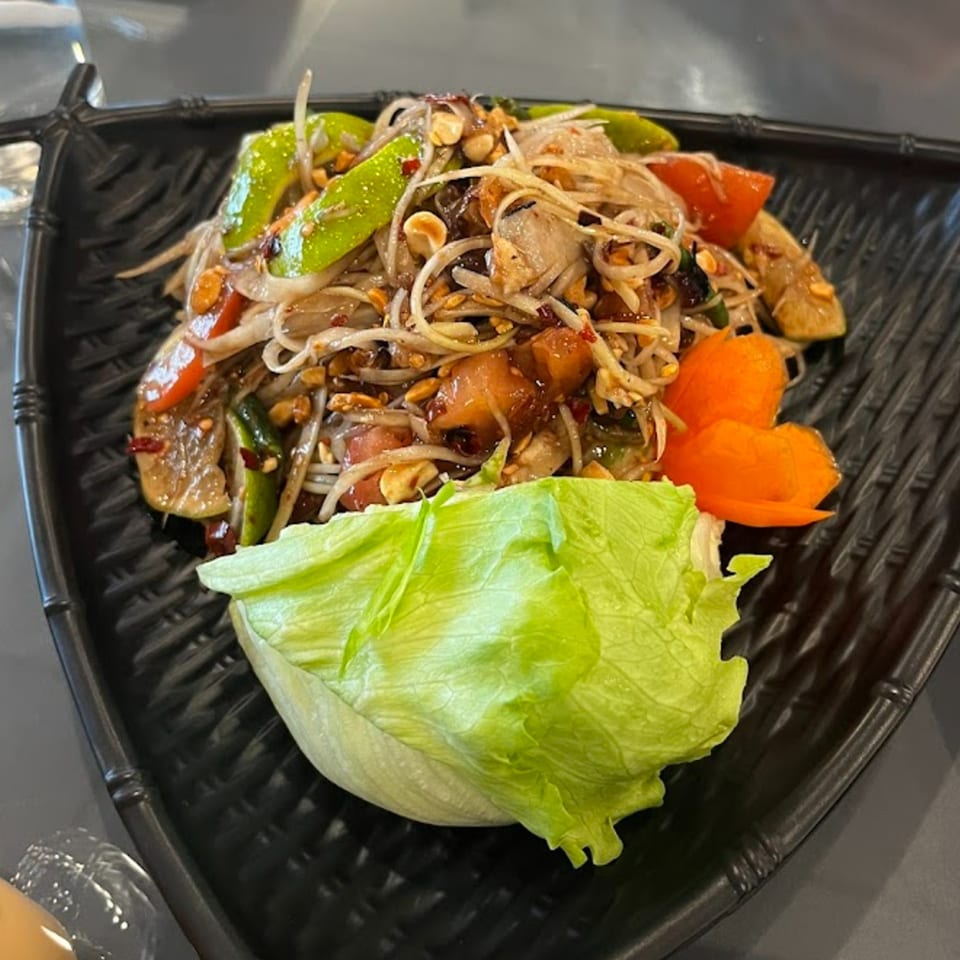 Som Tum (papaya salad) with peanuts, tomatoes, and green beans, served with lettuce and carrot garnish.