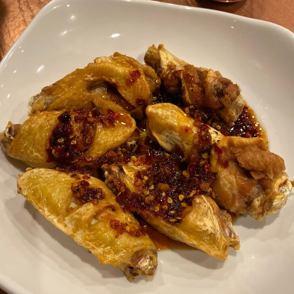 Golden-brown Thai chicken wings topped with a spicy chili garlic sauce on a white plate.