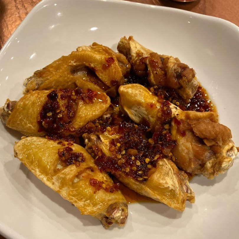 Golden-brown Thai chicken wings topped with a spicy chili garlic sauce on a white plate.