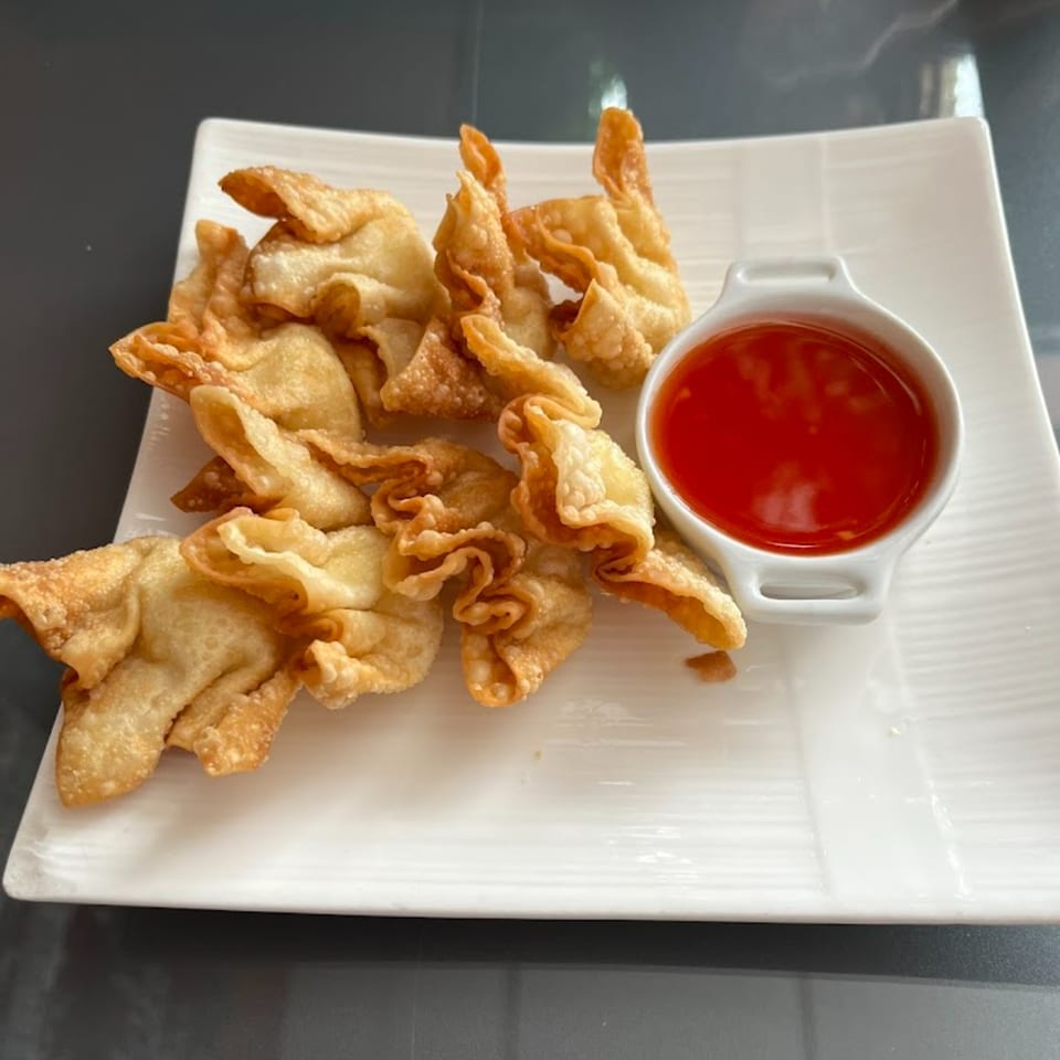 Crispy golden fried wontons with a side of sweet chili dipping sauce on a white rectangular plate.
