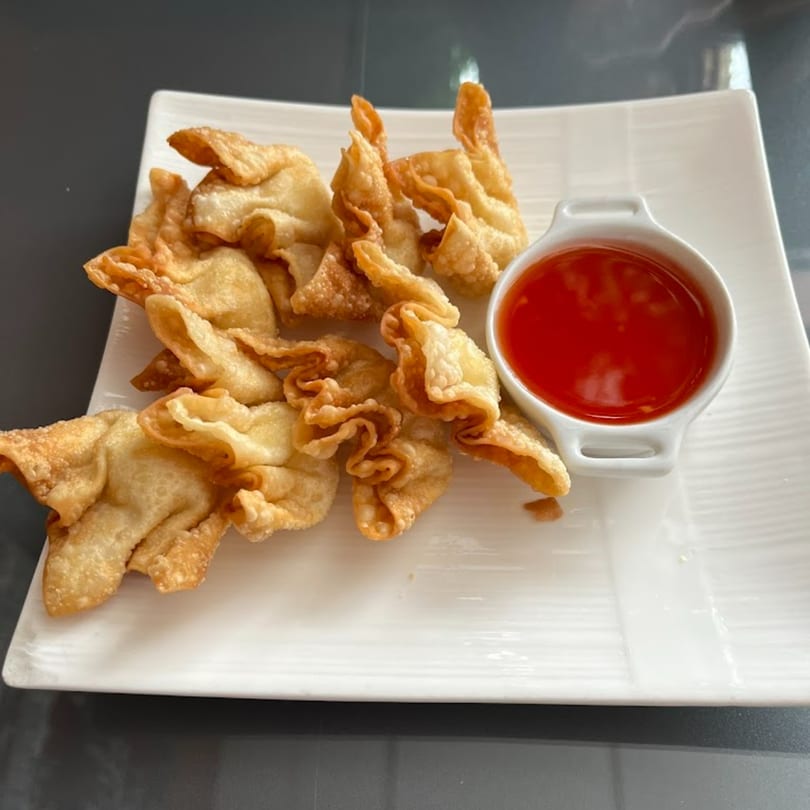 Crispy golden fried wontons with a side of sweet chili dipping sauce on a white rectangular plate.
