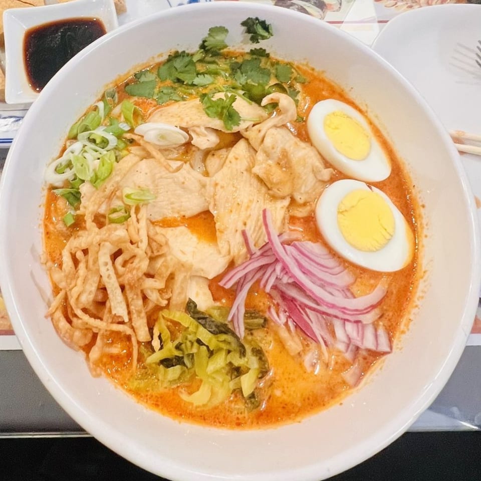 A bowl of Thai Khao Soi with chicken, crispy noodles, red onions, and hard-boiled eggs.