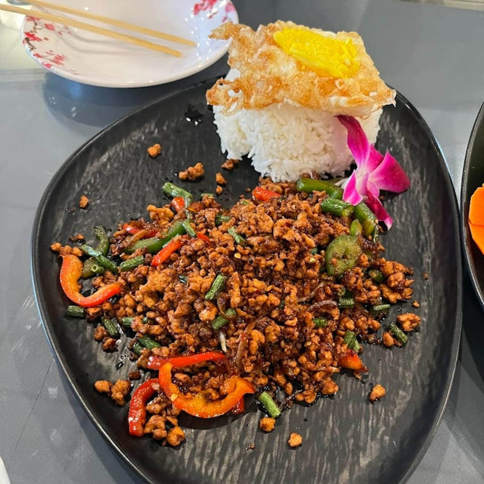 Thai basil chicken with rice and a fried egg, garnished with an orchid.